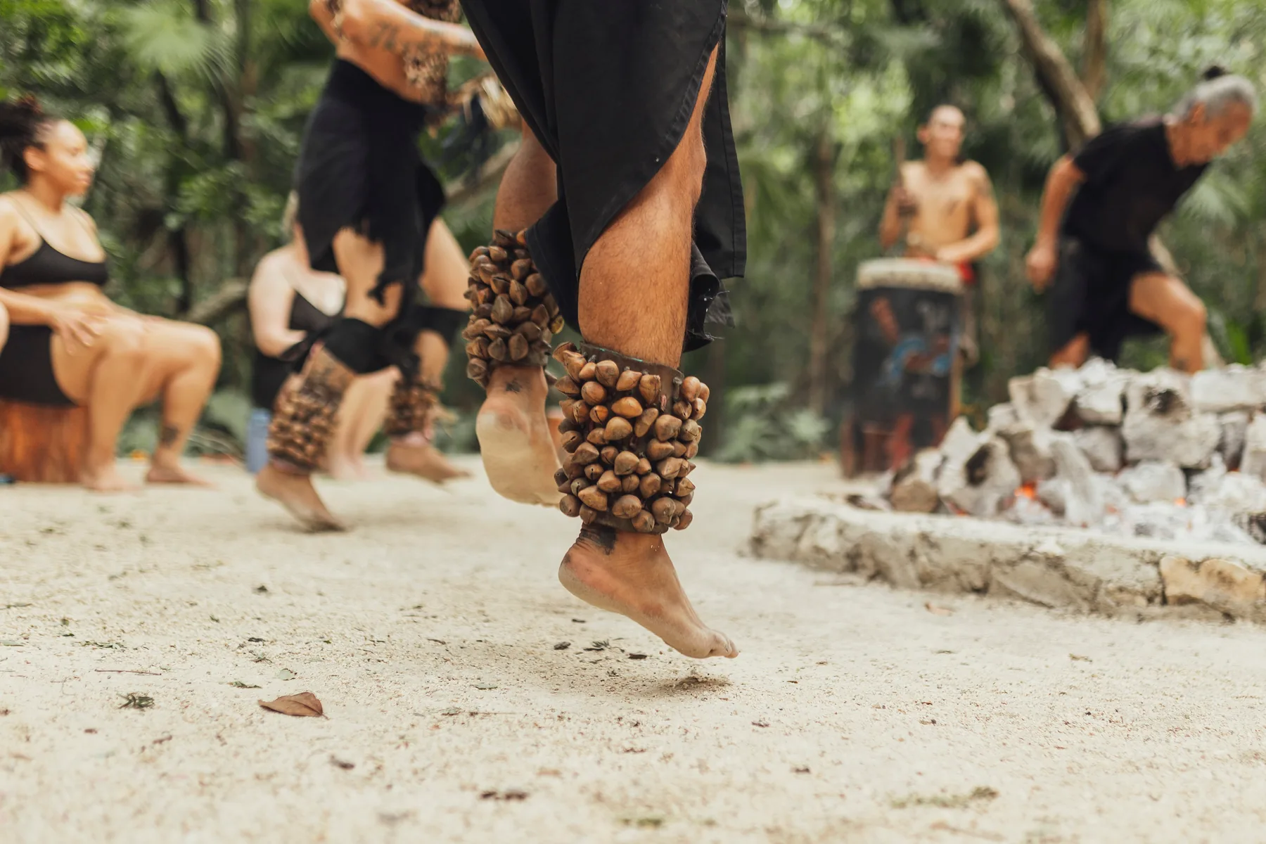 A fire ceremony in the Riviera Maya: dancers mid-step, seed-pod rattles at the ankle, a drummer behind