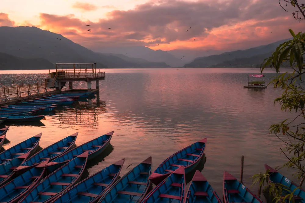 Phewa Lake at Pokhara after sunset, wooden boats moored along the shore beneath the hills